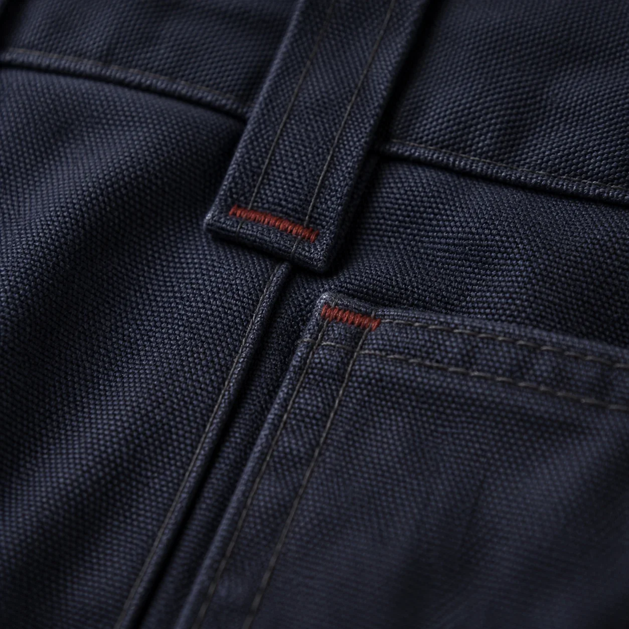 Oxide-red bar-tack reinforcements at a navy canvas pocket and belt loop